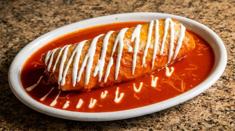 A large, saucy burrito drizzled with sour cream, served in a white oval dish.