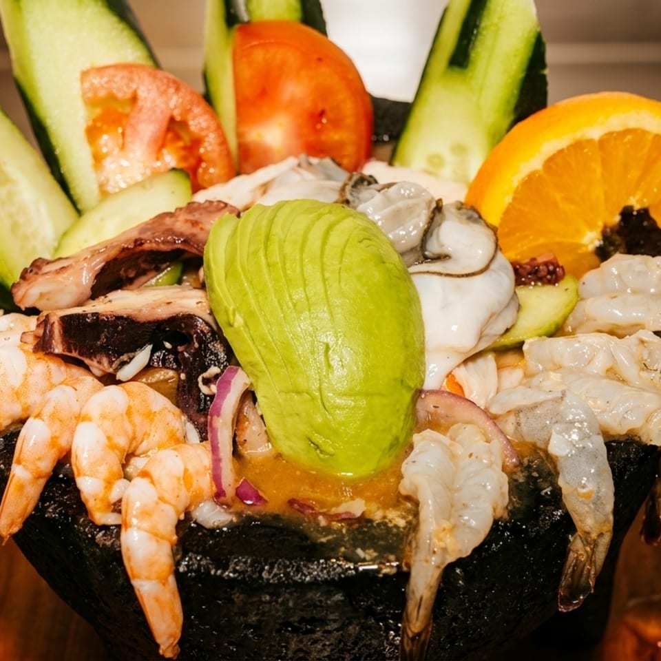 A vibrant seafood cocktail with shrimp, octopus, oysters, avocado, cucumber, tomato, and orange.