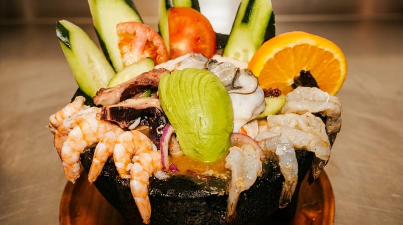 A vibrant seafood cocktail with shrimp, octopus, oysters, avocado, cucumber, tomato, and orange.